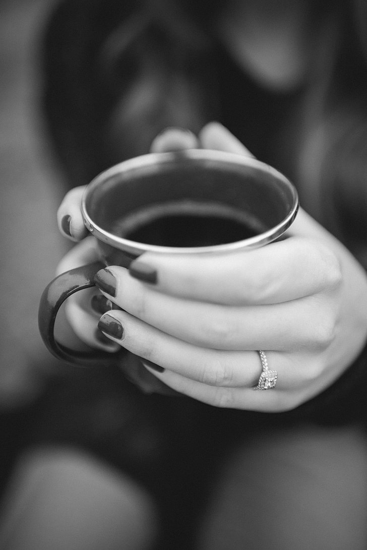 grayscale photo of woman wearing diamond ring holding ceramic cup with both hands