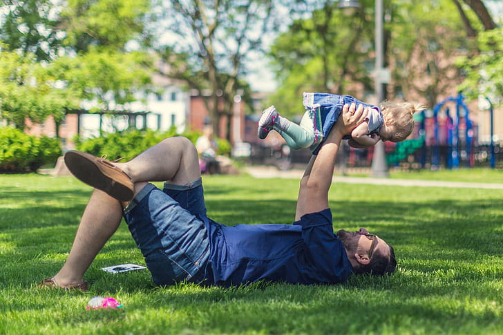 selective focus photography of man holding baby while lying on grass
