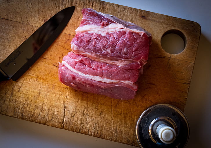 raw meat on brown wooden chopping board besides black kitchen knife