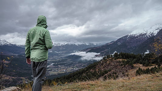 person wearing green jacket and gray pants standing in front mountain