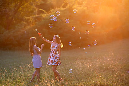 two women wearing mini dresses playing bubbles on grass field