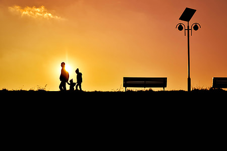 silhouette of three person walking near bench and post at sunset