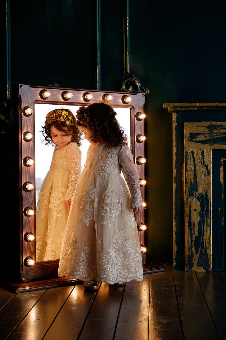girl wearing white floral embroidered dress looking at mirror