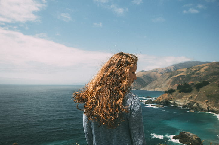 women's gray sweatshirt facing body of water and mountain view