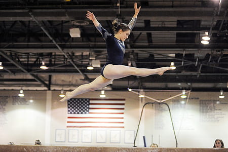 woman with black leotards jumping on brown balance beam