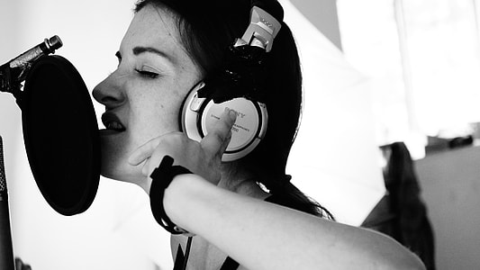 greyscale photo of woman wearing over-ear headphones near pop filter