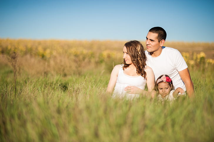 man, woman and child sitting on grass field during daytime