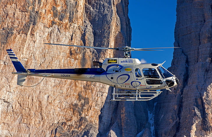 white and blue helicopter flies near brown rock formation