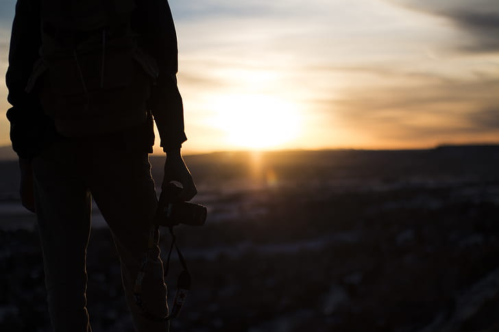 person holding camera while standing on top of the mountain during sunset