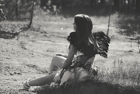 gray scale photo of a woman with black wings and white skirt sitting on ground