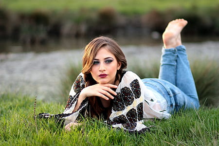 woman wearing black and white shirt and blue denim jeans reclining in grass