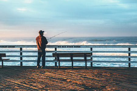 man wearing brown shirt and black pants holding fishing rod during daytime