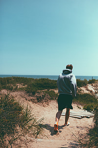 man wearing grey pull-over hoodie and black shorts standing on brown sand during daytime