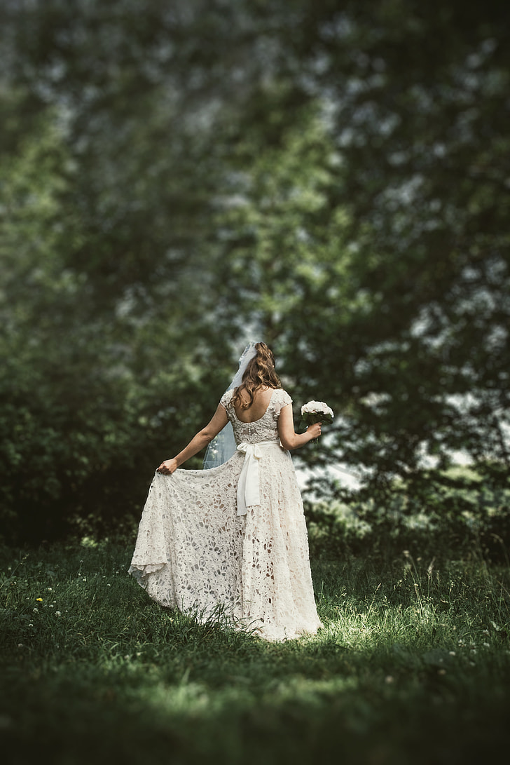 woman in white lace wedding dress holding a white bouquet surrounded with trees