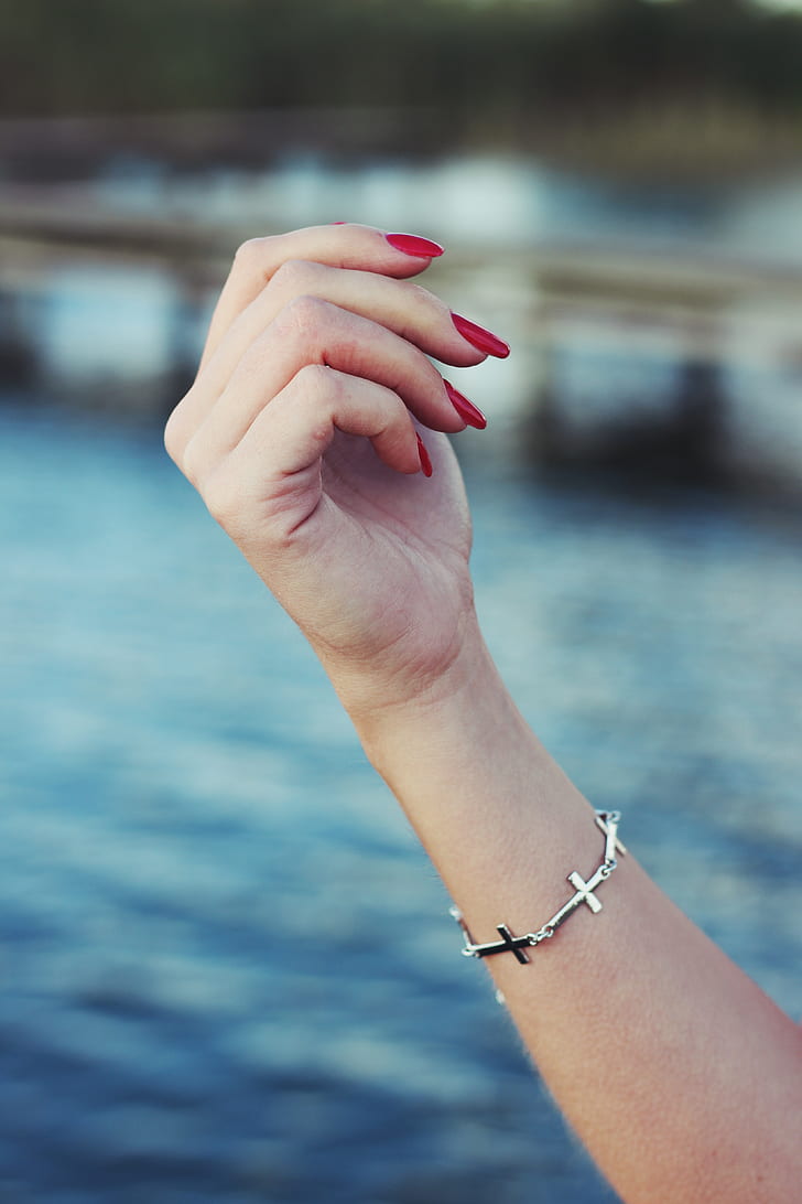 person with red manicure and silver-colored sideway cross bracelet