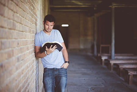 man leaning on wall reading book