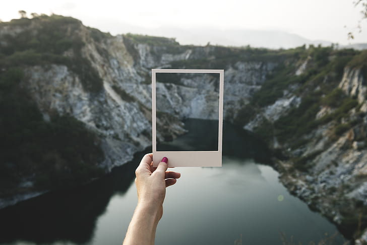 person holding white frame mirror facing mountain during daytime