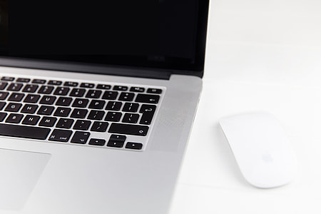 Apple Macbook Pro laptop computer and Magic Mouse situated on a minimalist pure white wood desk