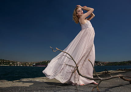 woman in white sleeveless dress standing behind body of water during daytime