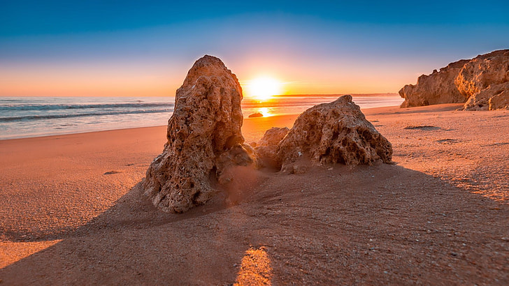 two brown rock formations near ocean during sunset