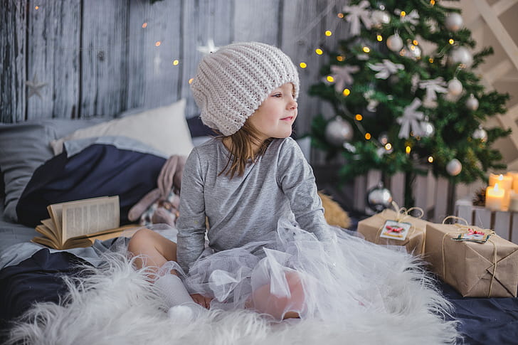 girl in gray long-sleeved shirt and knit cap sitting on white fur textile