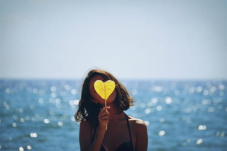 selective focus photography of woman holding yellow heart against sea shore