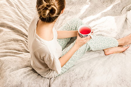 woman holding white cup sitting on bed