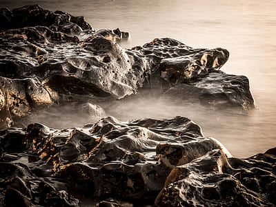brown and beige rocks on body of water with steam