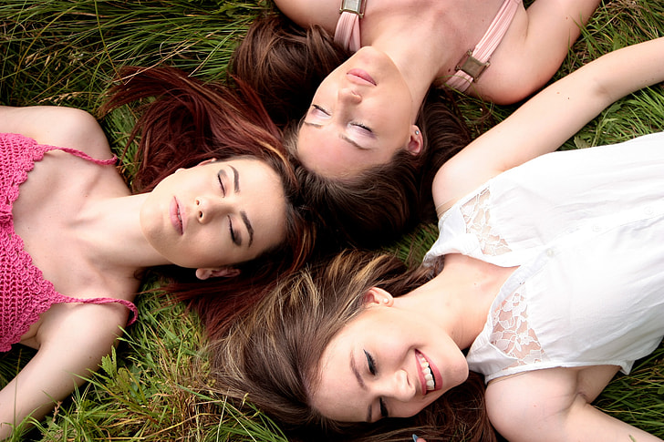 three women lying on green grass field during daytime