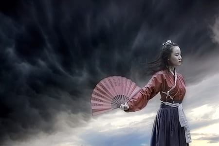 woman wearing purple and gray long-sleeved dress and holding hand fan with cloudy sky as background