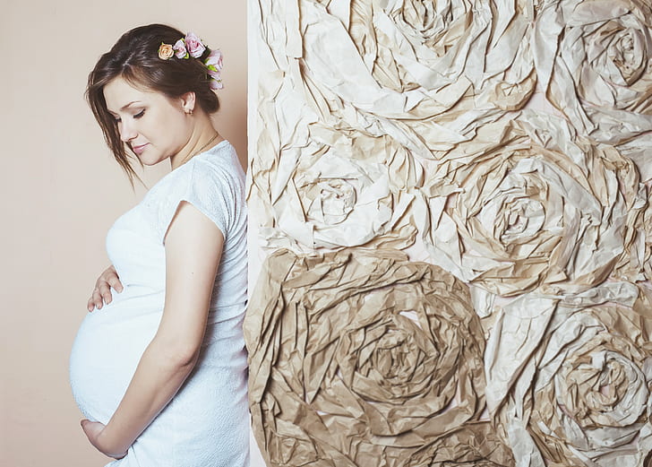 pregnant woman holding her tummy and leaning on brown wall
