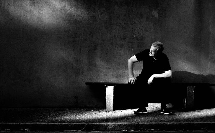 man wearing black shirt and black pants sitting on bench near wall