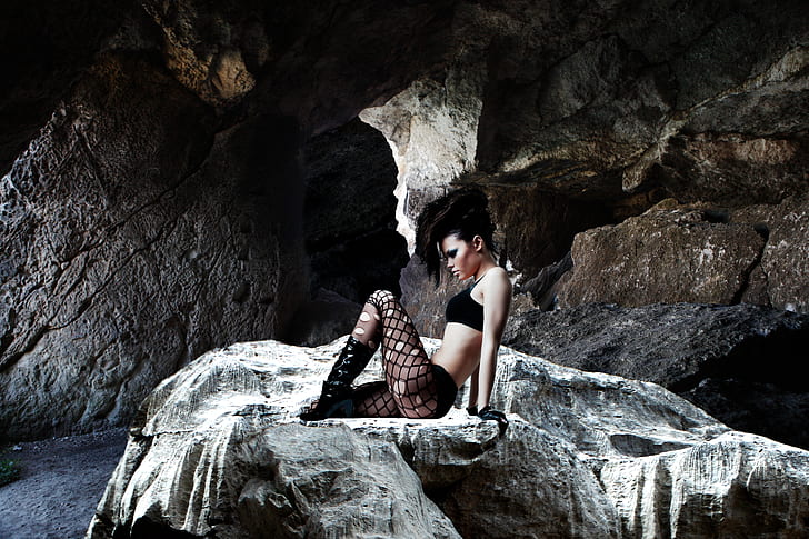 photo of woman sitting on rock in cave