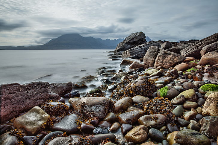 stones on seashore near mountains under cloudy sky during daytime