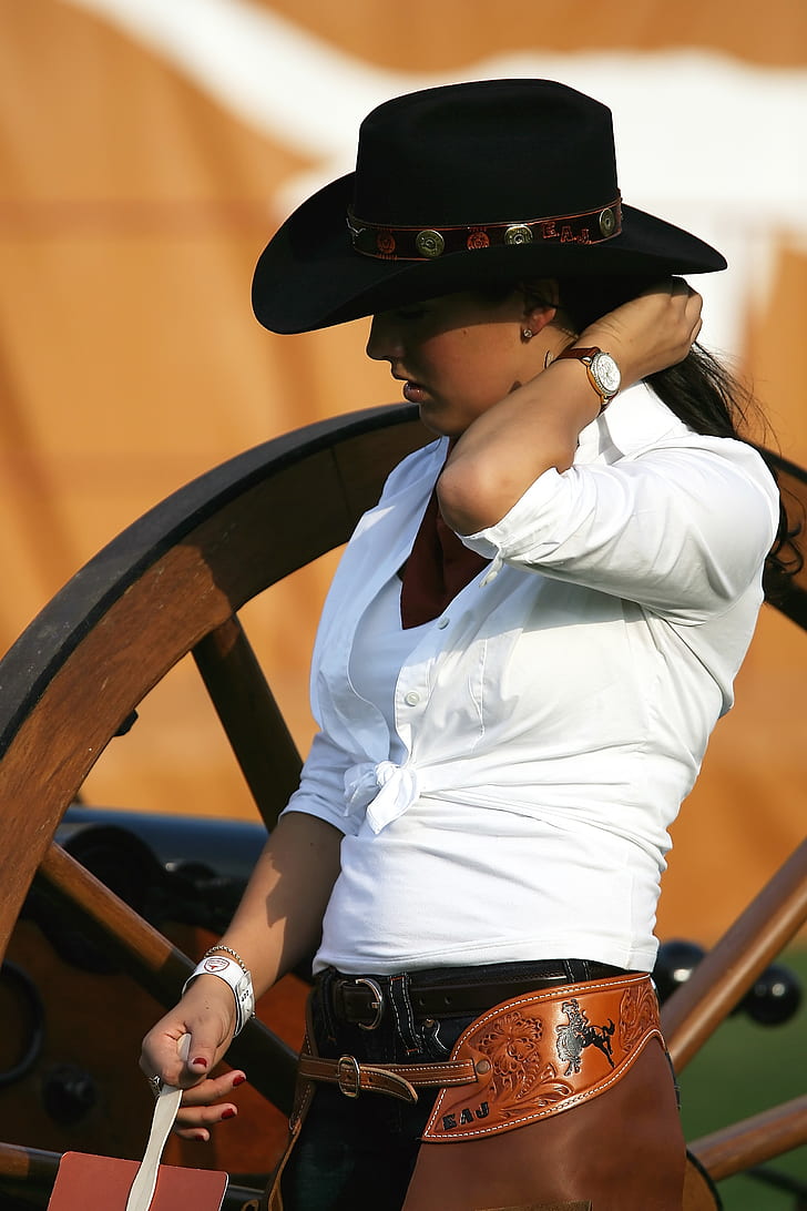 woman in white collared button-up long-sleeved dress shirt and black cowboy hat standing brown wooden frame at daytime