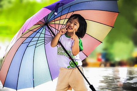 girl in white and green crew-neck t-shirt and brown shorts outfit smiling and holding multicolored umbrella