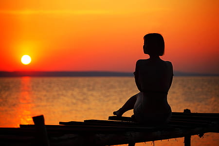 Silhouette of Woman Sitting on Dock during Sunset