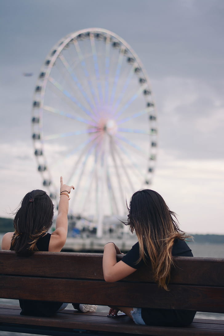 two women sitting on bench pointing on London Eye Ferris wheel