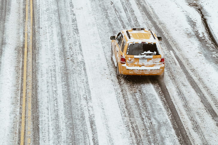 yellow taxi cab on snow filled asphalt road