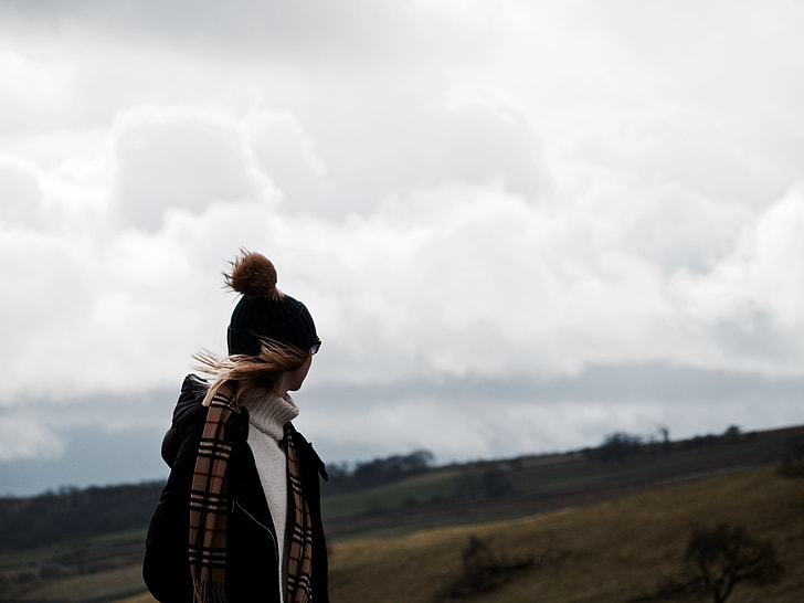 person in bobble cap and jacket with burberry scarf standing in open field area