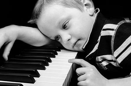 grayscale photograph of boy laying on piano keyboard