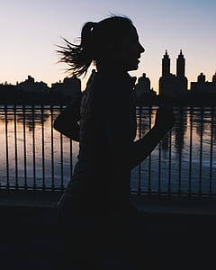 silhouette photo of woman running beside body of water