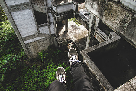 human wearing black pants and pair of gray Vans Old Skool sitting on cliff of abandoned concrete house