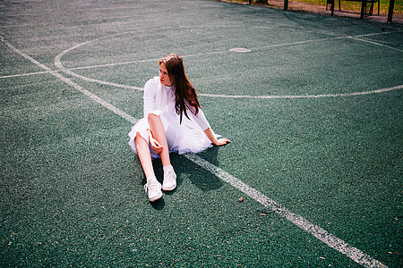 woman wearing white dress and pair of sneakers sitting on field