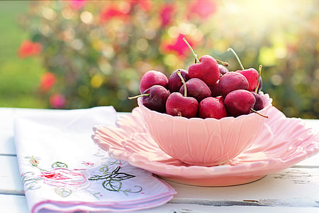 pink bowl of red cherry fruits beside pink floral cloth