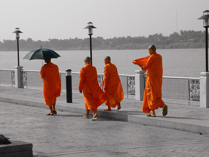 four monk walking near gray metal road railings near body of water