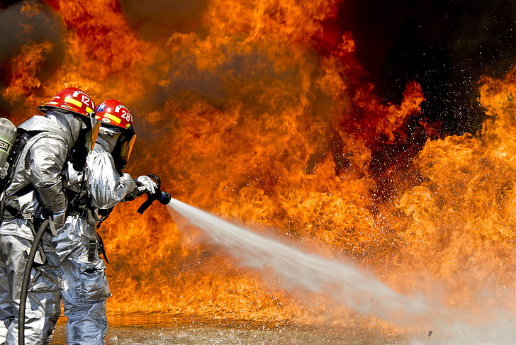firefighters wearing silver suits spraying foam on fire