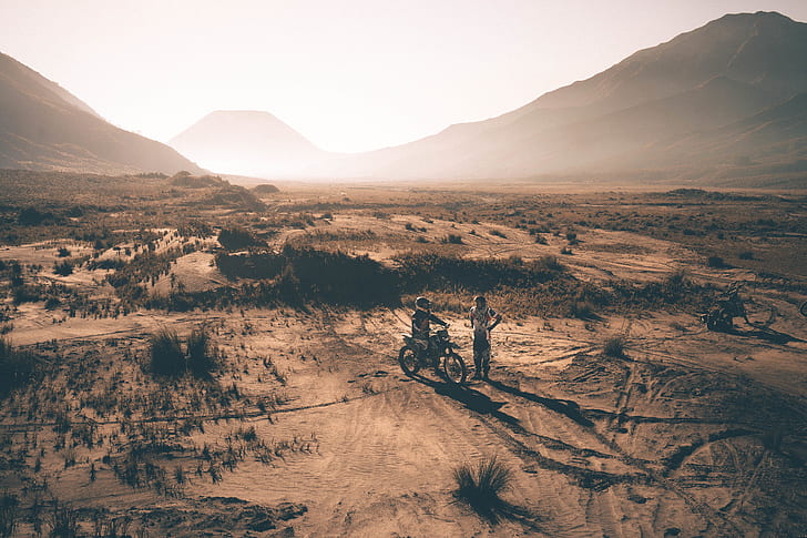 two people on desert with dirt bike photo taken during golden hour