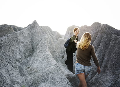 woman reaching other woman between rocks