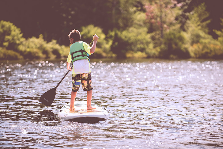 boy in green vest on white and black paddle boat on body of water during daytime